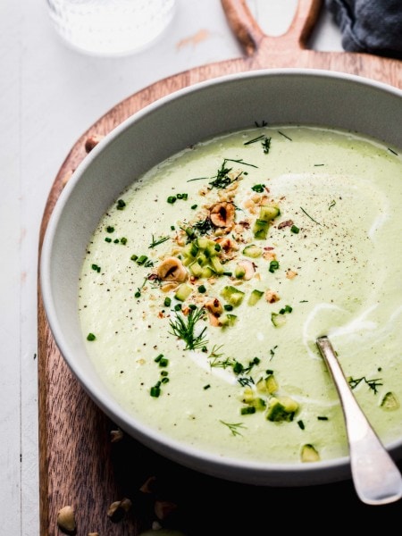 Side view of bowl of chilled cucumber soup with spoon and topped with hazelnuts.