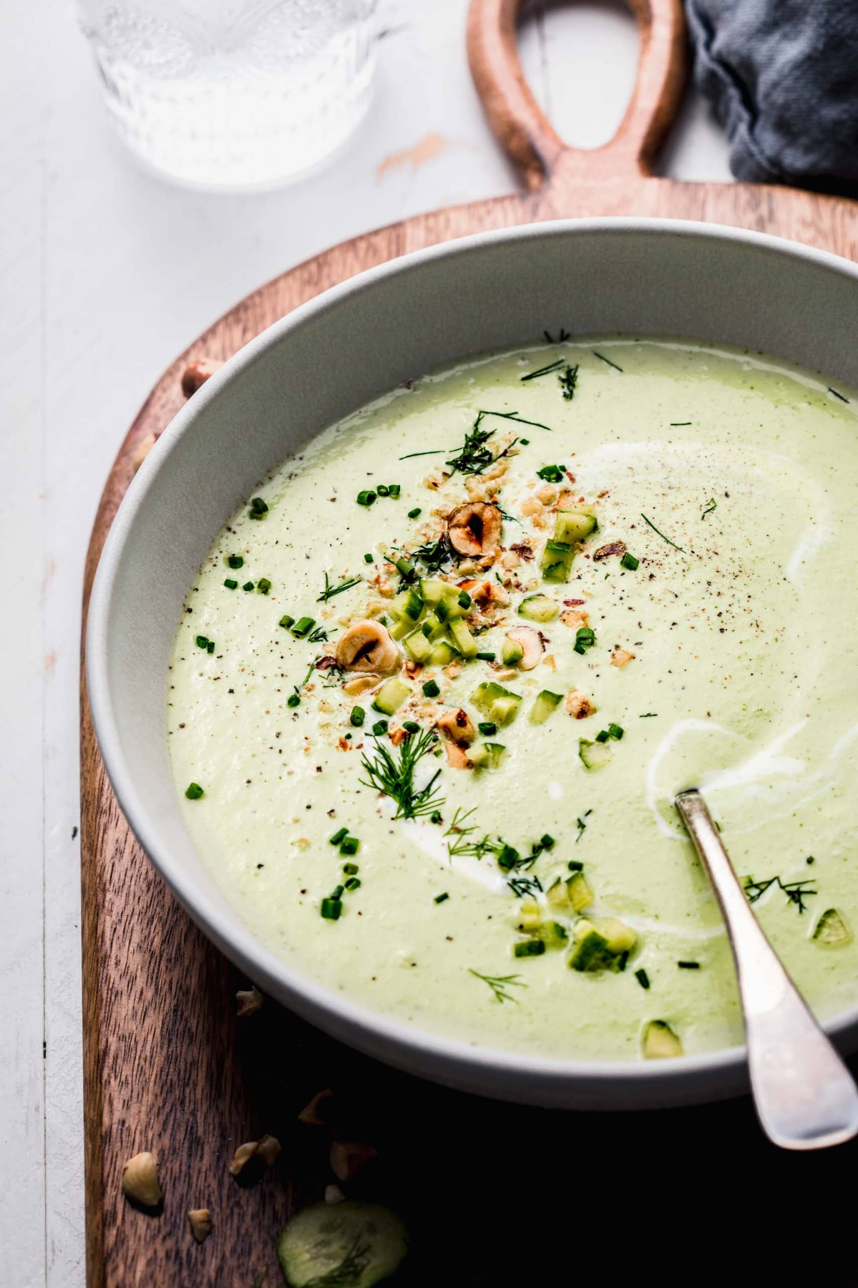 Side view of bowl of chilled cucumber soup with spoon and topped with hazelnuts.