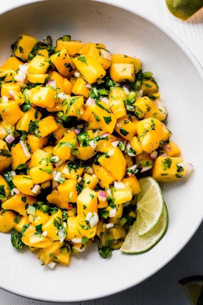 MANGO SALSA IN WHITE BOWL WITH LIME WEDGES.