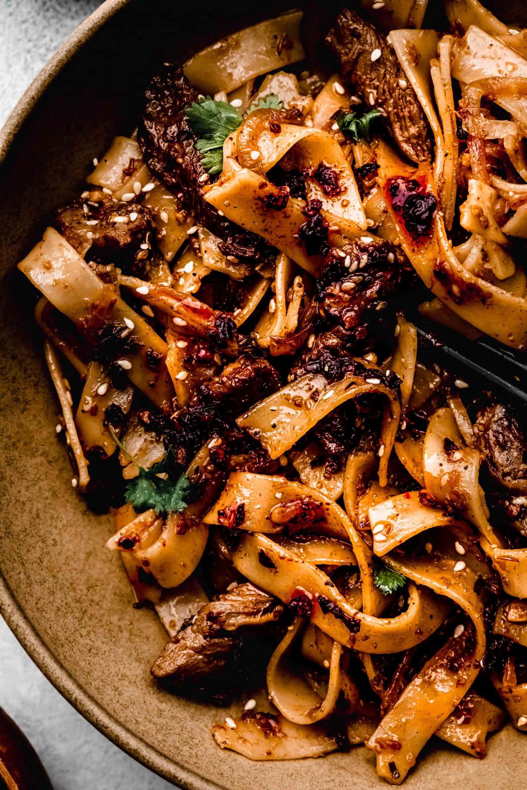 Overhead close up of cumin lamb noodles in brown bowl with chopsticks.