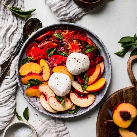 Overhead shot of peach caprese salad on grey plate next to wooden cutting board.