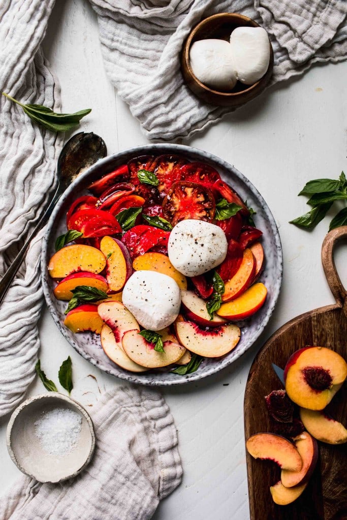 Overhead shot of peach caprese salad on grey plate next to wooden cutting board.