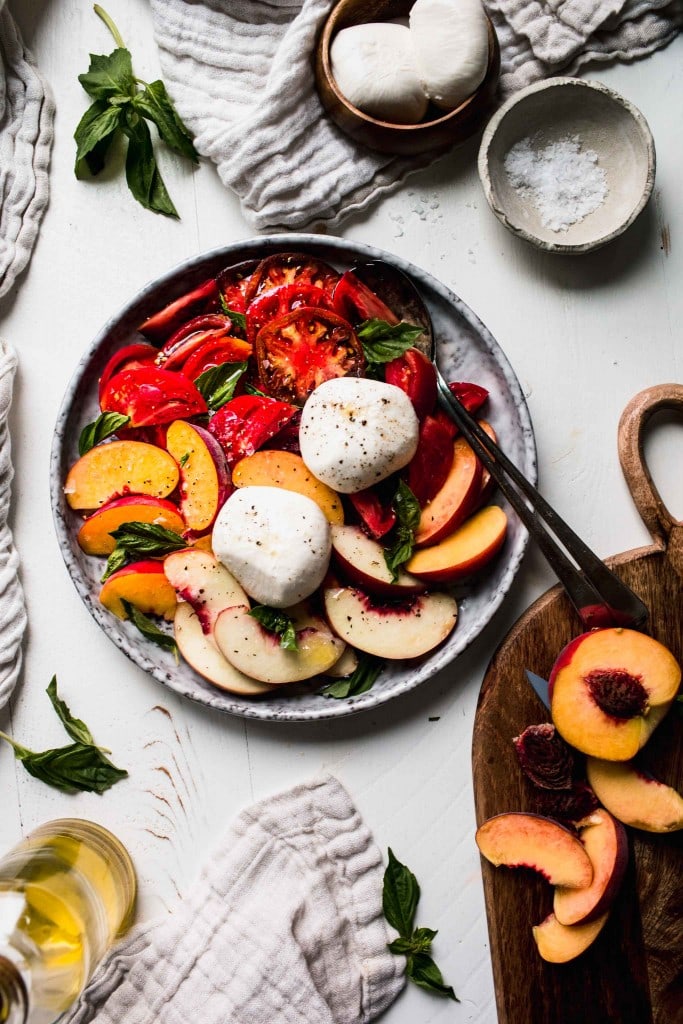 Overhead shot of peach caprese salad on grey plate next to wooden cutting board.