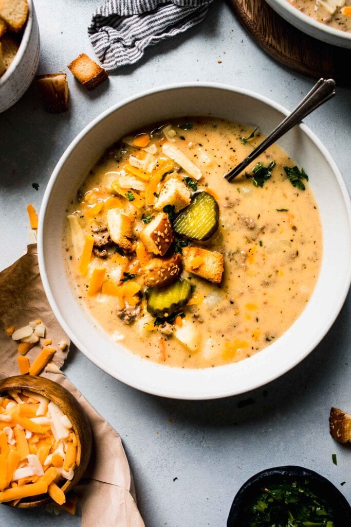 BOWL OF CHEESEBURGER SOUP TOPPED WITH PICKLE SLICES.