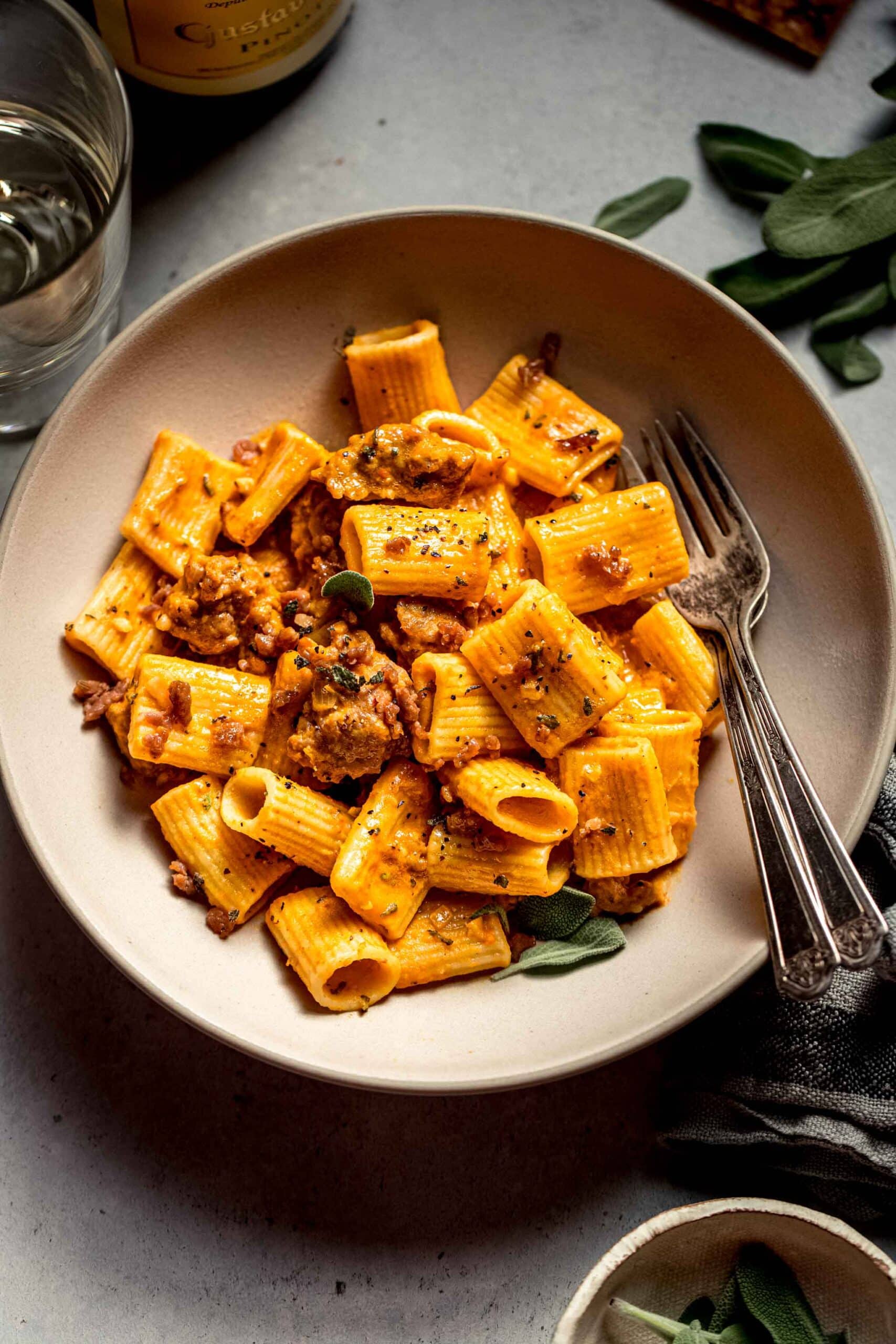 Overhead shot of bowl of pumpkin pasta flecked with sage leaves.