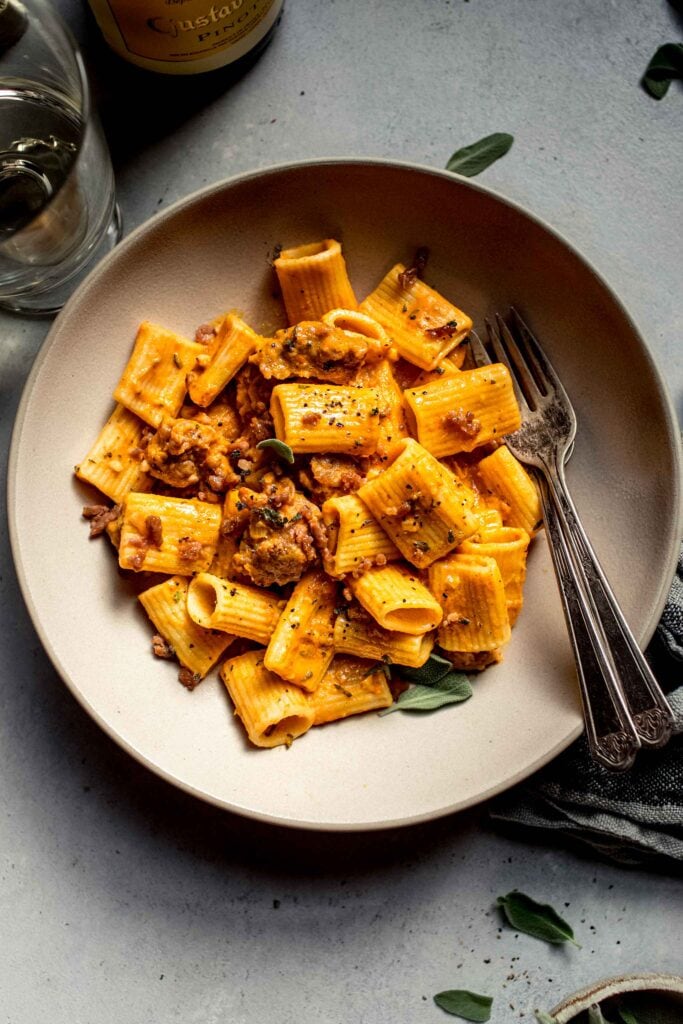 Overhead shot of bowl of pumpkin pasta flecked with sage leaves.