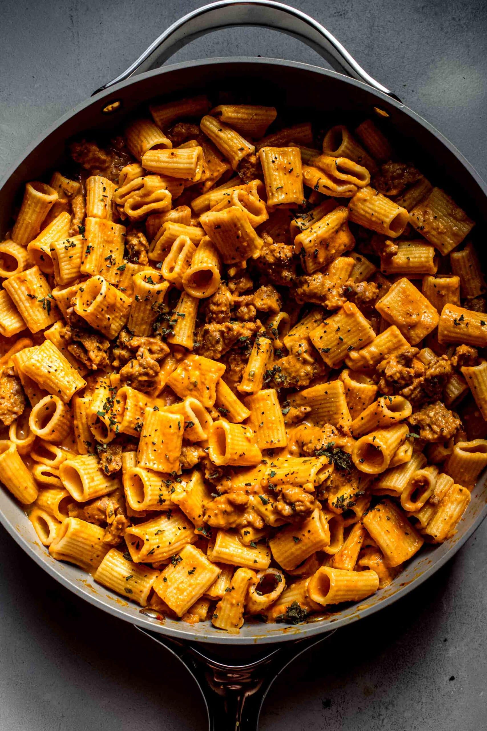 Pasta tossed with pumpkin sauce in skillet.