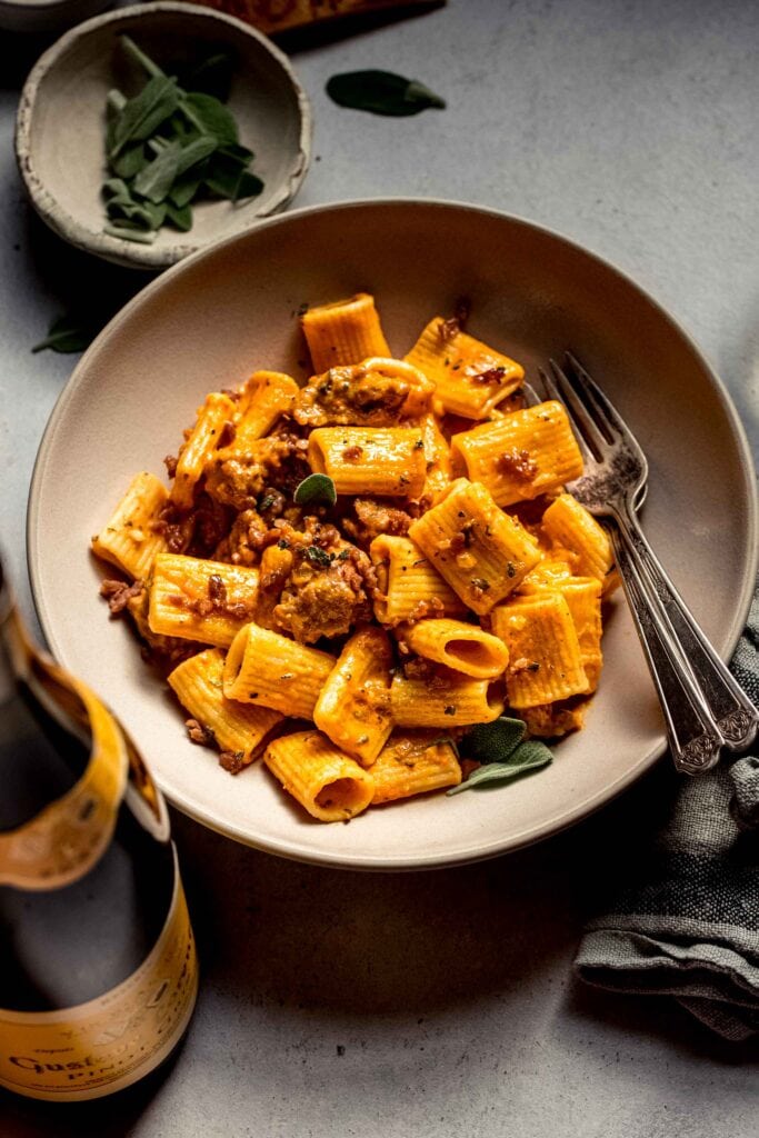 Bowl of pumpkin pasta next to bottle of wine. 