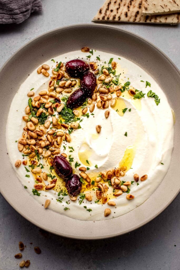 Bowl of whipped feta with swirl of olive oil, kalamata olives and pine nuts. 