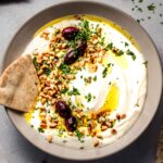 Whipped feta dip in bowl topped with olives, pine nuts and olive oil. Served with pita.