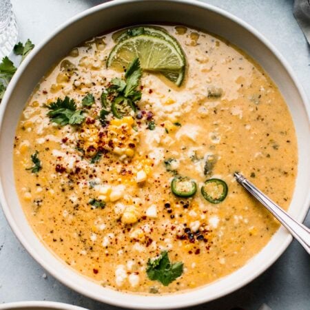 Bowl of Mexican Corn Soup garnished with cliantro, chile powder and lime wedges.