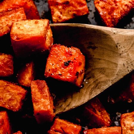 CLOSE UP OF ROASTED SWEET POTATOES ON SERVING TRAY WITH SPOON.