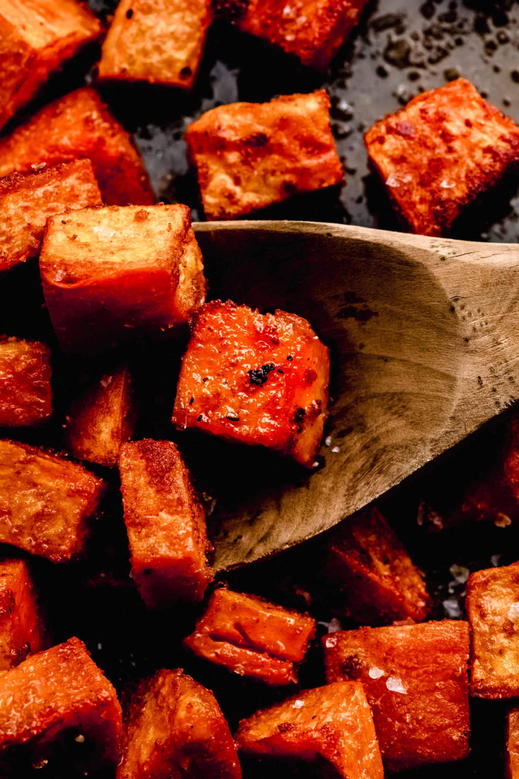 CLOSE UP OF ROASTED SWEET POTATOES ON SERVING TRAY WITH SPOON.