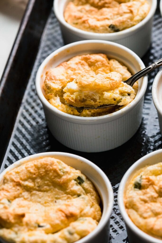 Several ramekins of spoon bread on tray with spoon. 