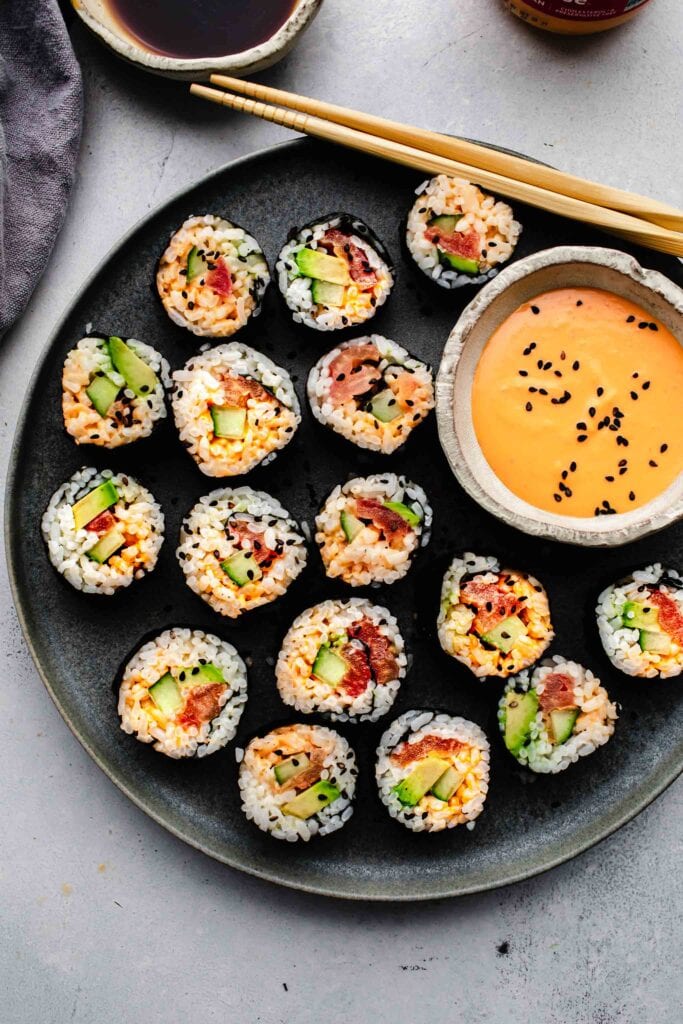 Vegetarian sushi rolls arranged on plate with bowl of spicy mayo. 