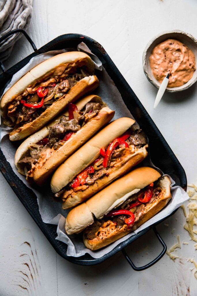 Cheesesteaks in tray next to bowl of chipotle mayo. 