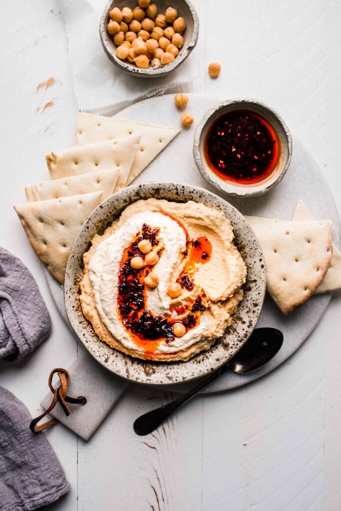 Whipped feta hummus on serving platter next to pita and bowl of chili oil. 