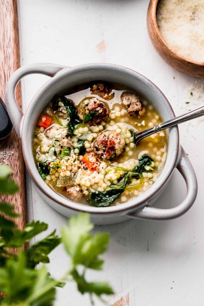 Italian wedding soup in small grey bowl with parmesan.