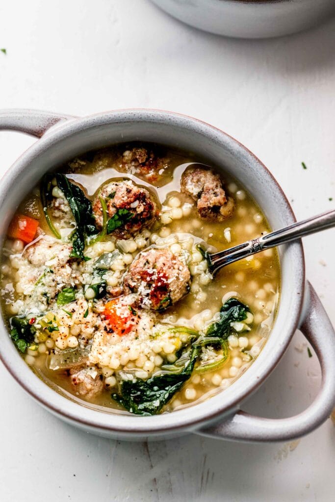Bowl of wedding soup with spoon and topped with parmesan. 