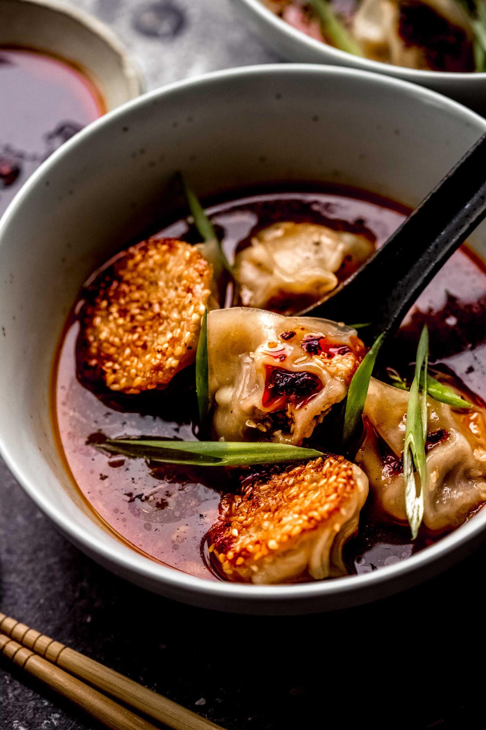 CLOSE UP OF BOWL OF LAMB DUMPLINGS IN SPICY GINGER BROTH.