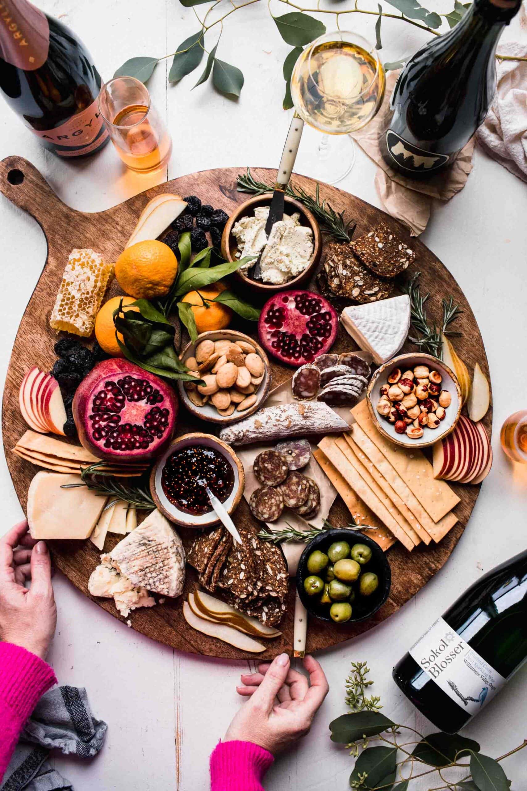 Hands holding large cheese platter set next to sparkling wines.
