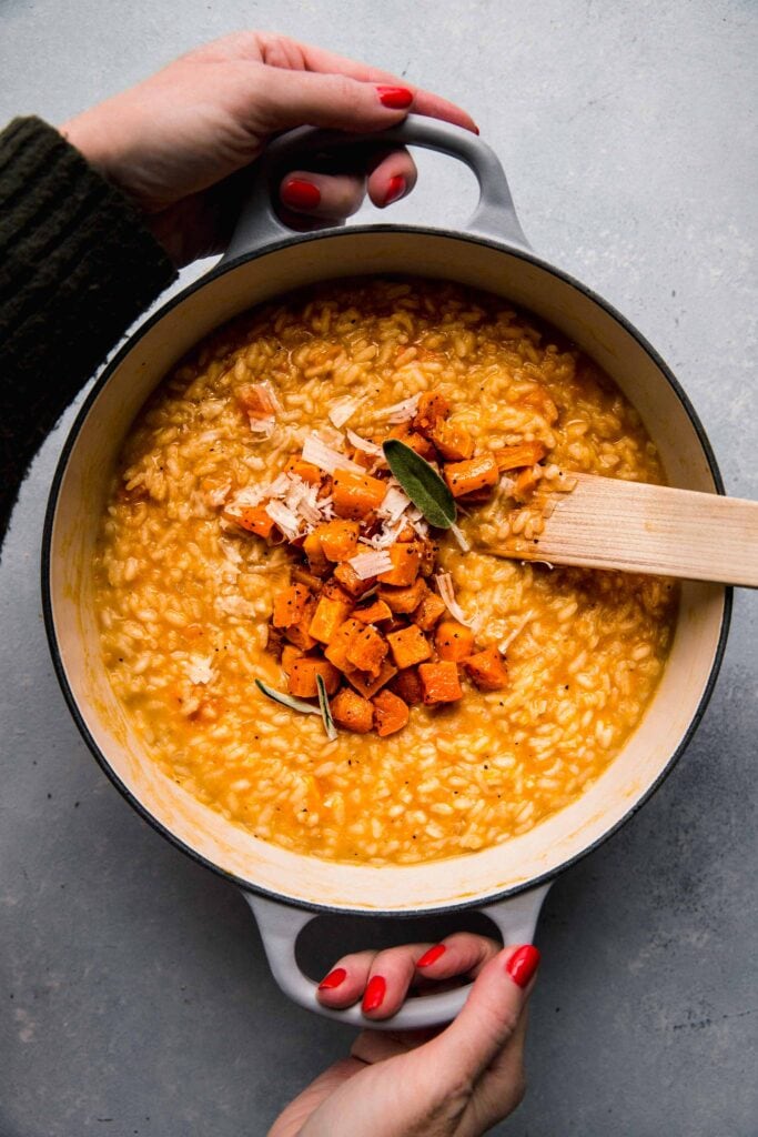 Hands holding pot of butternut squash risotto.