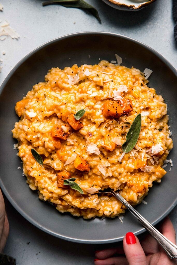 Overhead shot of hand holding bowl of butternut squash risotto.