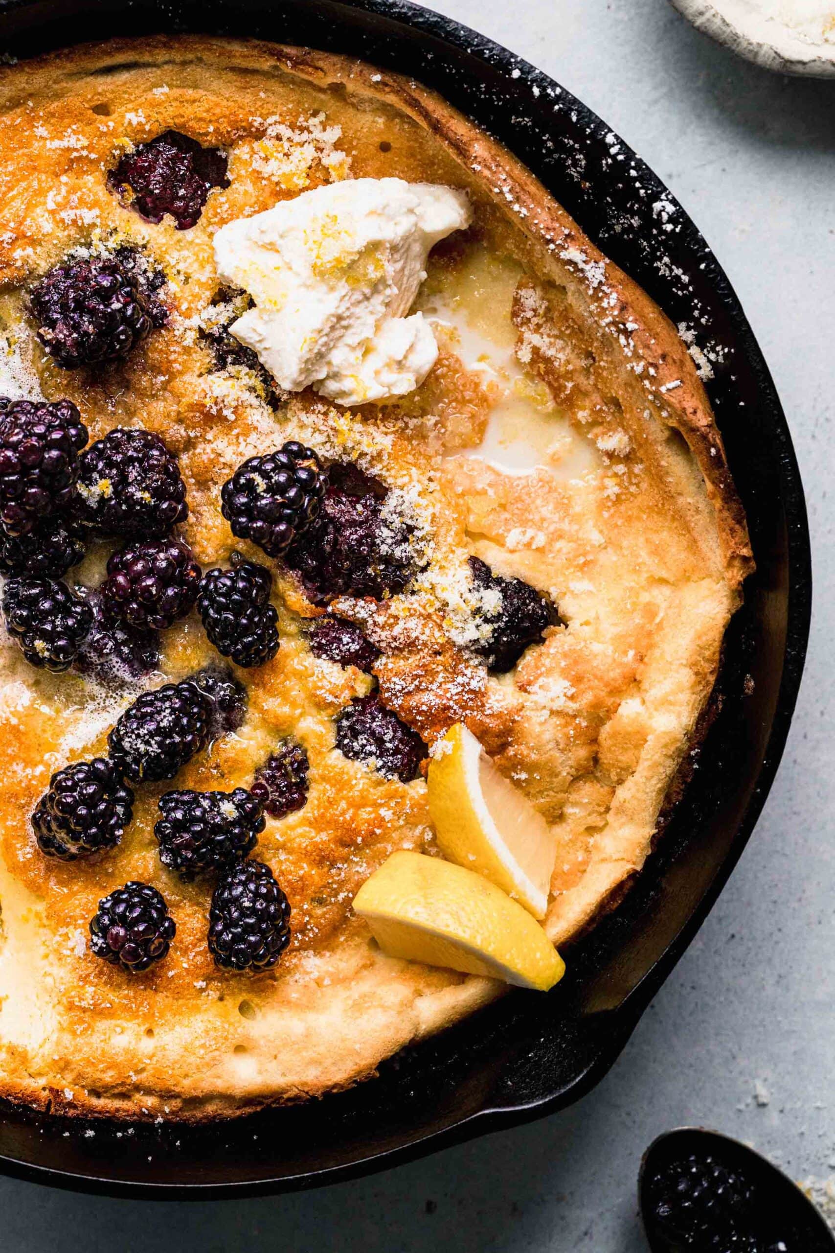 Dutch baby pancake in cast iron skillet topped with blackberries and lemon wedges.