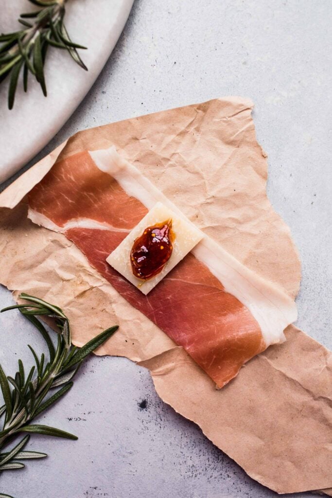 Half slice of prosciutto topped with cheese and figs before wrapping. 