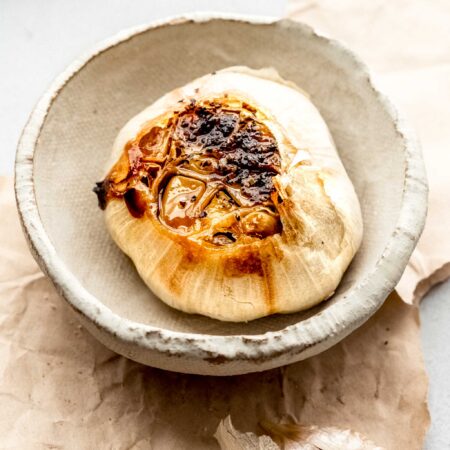 HEAD OF ROASTED GARLIC IN SMALL SERVING DISH.
