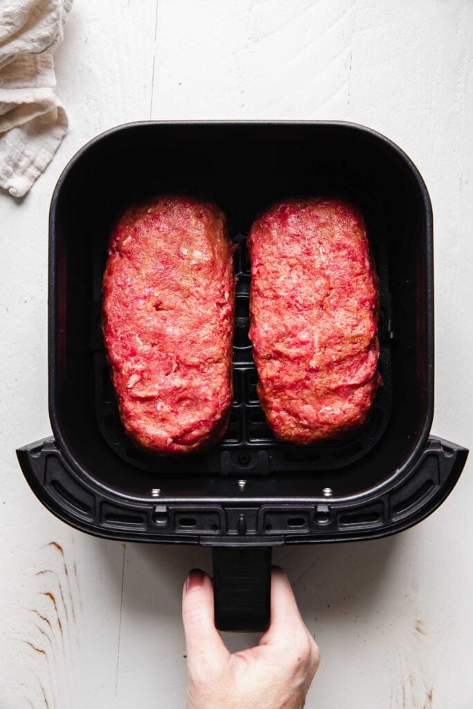 Two uncooked meatloaves in air fryer basket. 