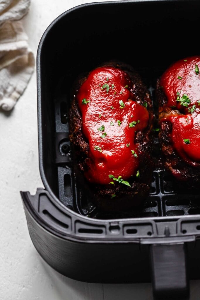 Two cooked meatloaves in air fryer basket sprinkled with parsley. 