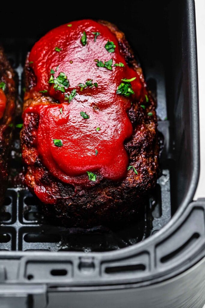 Meatloaf in air fryer basket topped with tomato sauce & parsley.