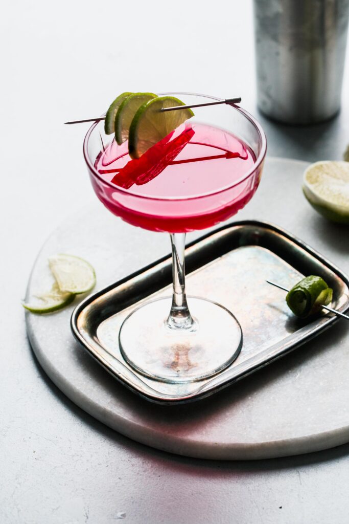 Cosmopolitan cocktail garnished with lime slices on cocktail pick.