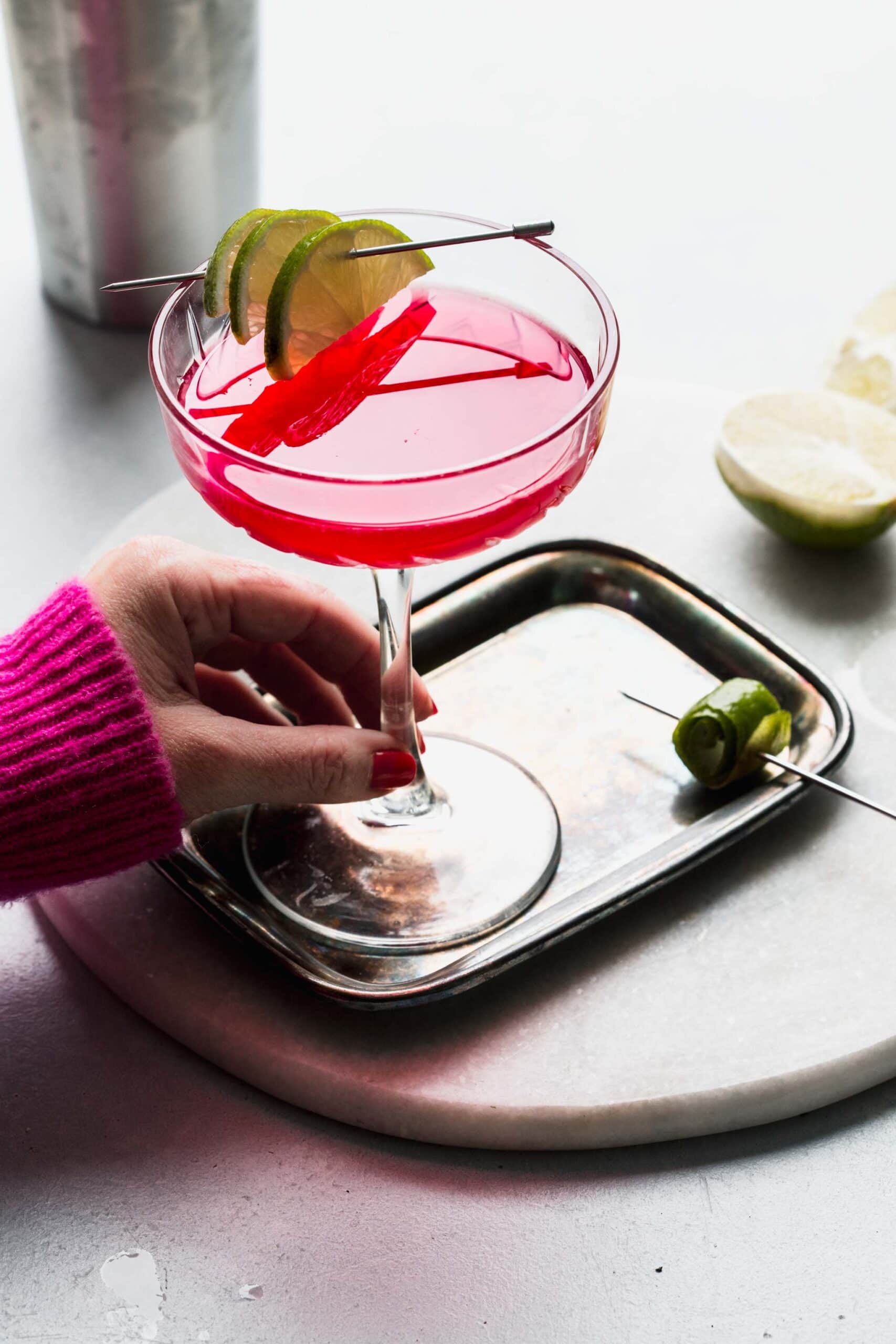 Hand holding cosmo cocktail in coupe glass.
