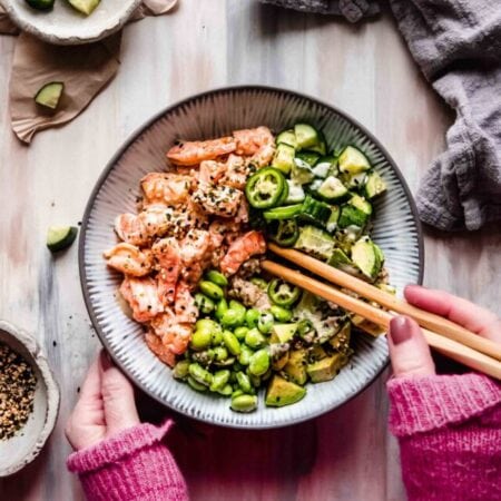 Hands holding shrimp sushi bowl.