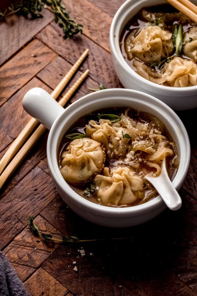 Two bowls of french onion soup dumplings next to chopsticks. 