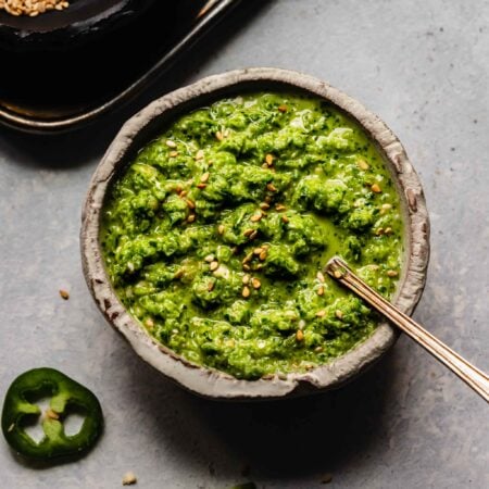 Bowl of jalapeno salsa next to small bowl of sesame seeds.