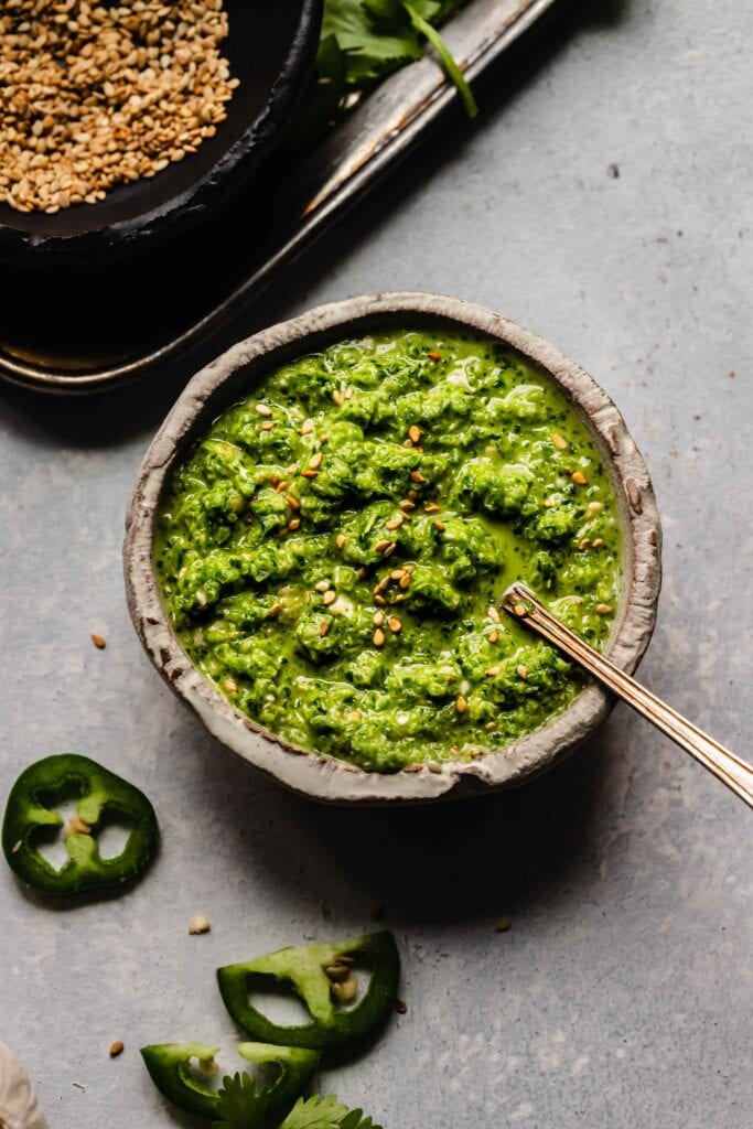 Bowl of jalapeno salsa next to small bowl of sesame seeds.