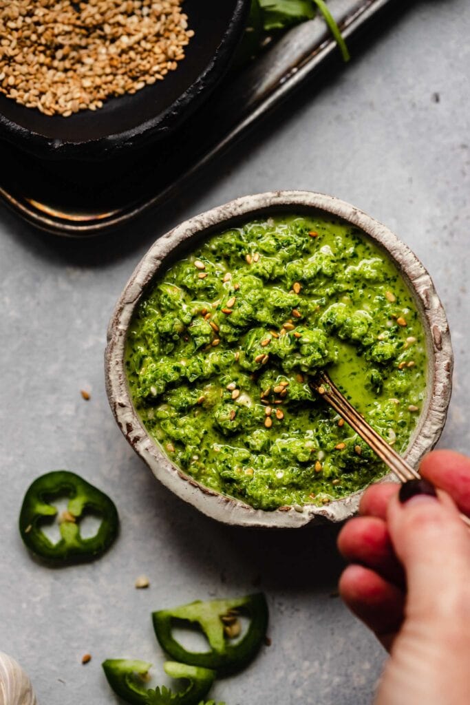 Hand dipping spoon into jalapeno sesame salsa. 