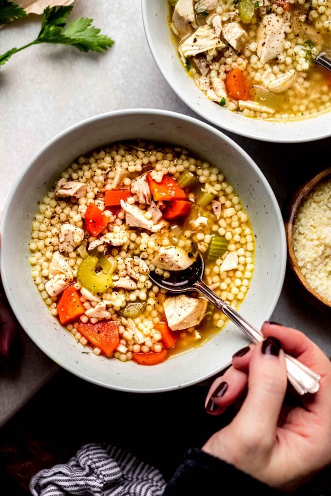 Hand dipping spoon into bowl of leftover chicken soup.