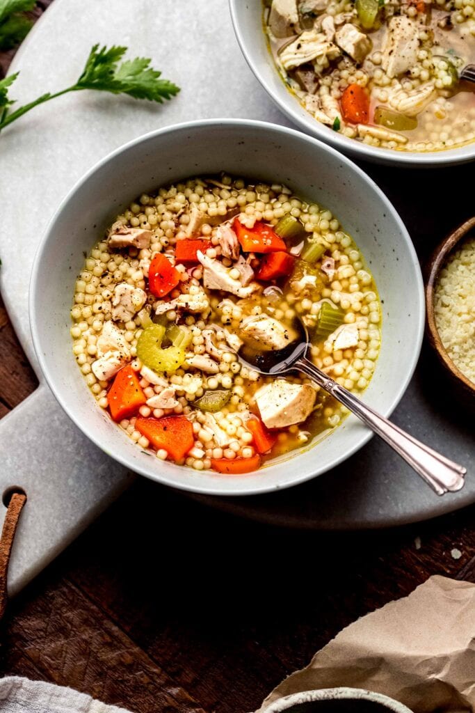 Two bowls of chicken carcass soup with spoon.