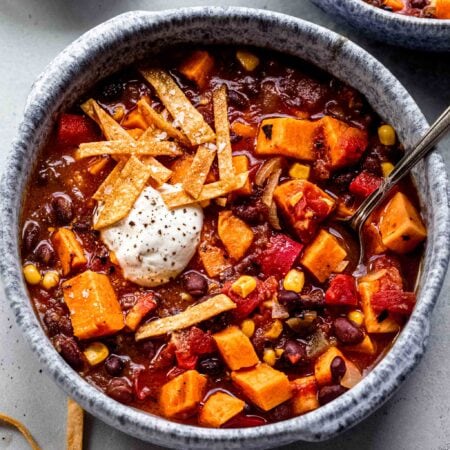 Sweet potato chili in blue bowl topped with tortilla strips and sour cream.