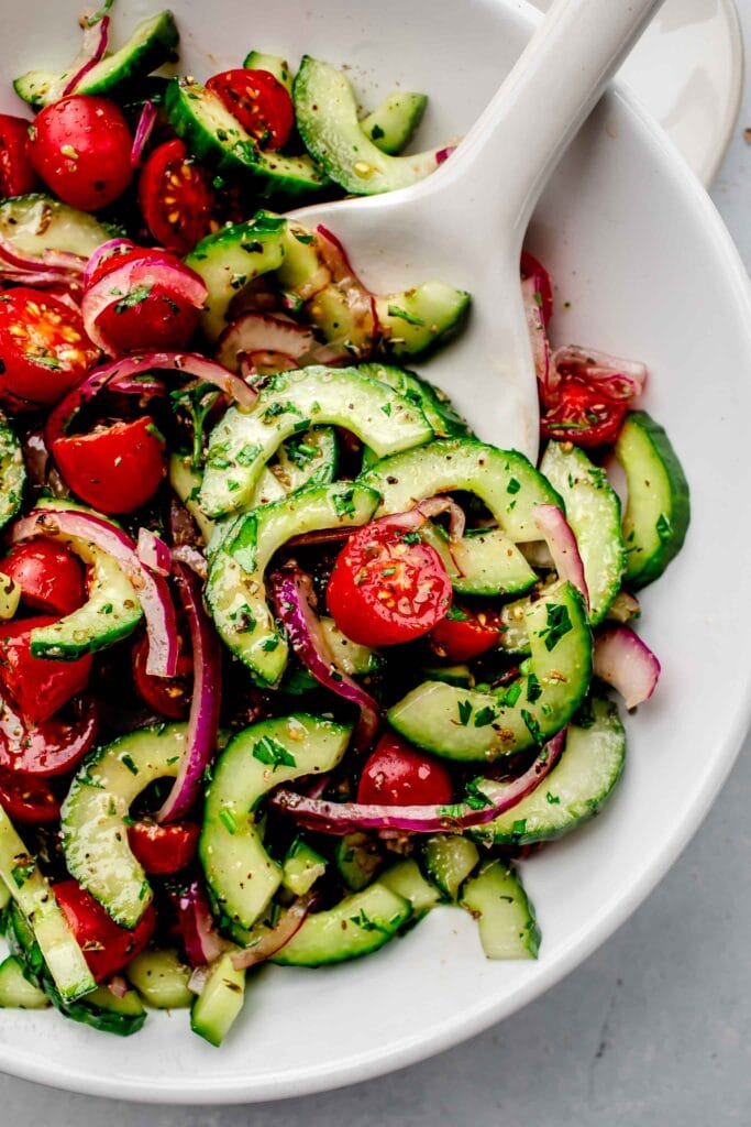 Tomato cucumber salad in white serving bowl with spoon. 