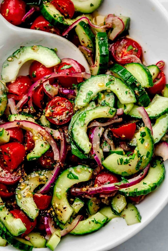 Serving spoon in bowl of tomato cucumber salad.