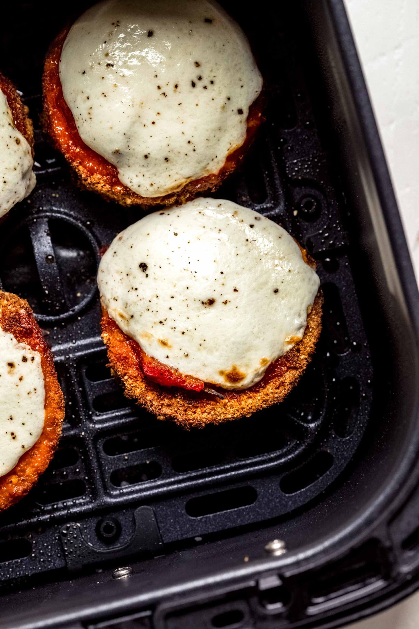 Eggplant slices topped with mozzarella and marinara in air fryer basket. 