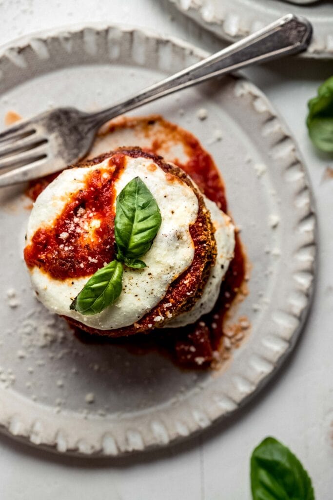 Overhead shot of Eggplant parmesan stacked on plate and topped with basil leaves. 