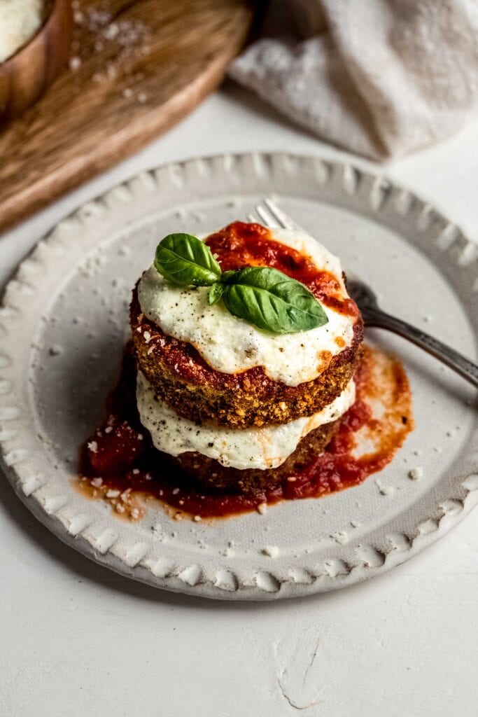 Eggplant parmesan stacked on plate and topped with basil leaves.