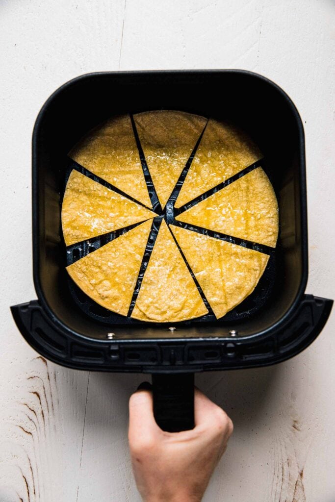 Tortilla cut into wedges in air fryer basket. 
