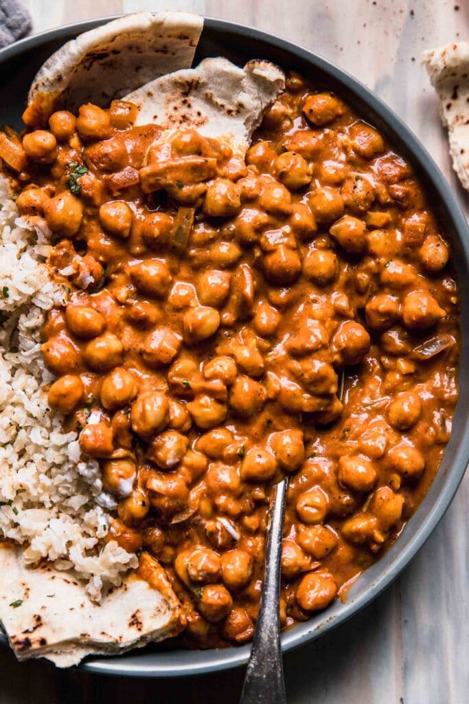 Overhead close up of butter chickpeas in grey bowl with rice and spoon. 